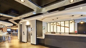 A modern reception area with a counter, seating, and an elevator. - Radisson Hotel Paris Le Bourget (Bonneuil-en-France)