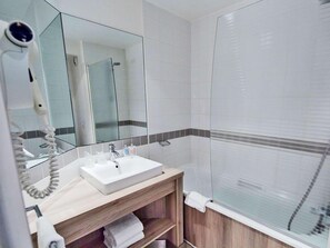 Un baño moderno con lavamanos blanco, espejo, secador de pelo y cabina de ducha.