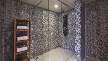 Une douche dont les murs sont recouverts de mosaïques, une étagère en bois avec des serviettes et une paroi en verre.
