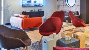 A modern living room with a sofa, red chairs, a TV, and a decorative wall. - Radisson Hotel Paris Le Bourget (Bonneuil-en-France)