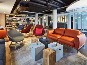 A modern lounge area with seating, a bookshelf, and a reception desk. - Radisson Hotel Paris Le Bourget (Bonneuil-en-France)