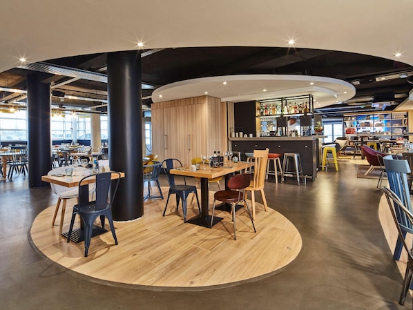 A modern restaurant with round tables, black and wooden chairs, a bar area, and a view of the parking lot. - Radisson Hotel Paris Le Bourget (Bonneuil-en-France)