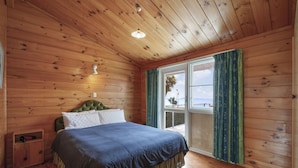 A wooden cabin bedroom with a bed, a nightstand, and a window with curtains.