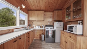 A compact kitchen with wooden cabinets, a sink, a stove, a refrigerator, and a microwave.