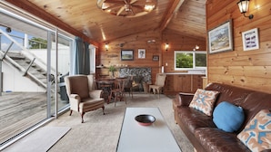 A cozy cabin interior with a stone fireplace, wooden walls, a dining area, and a leather sofa.