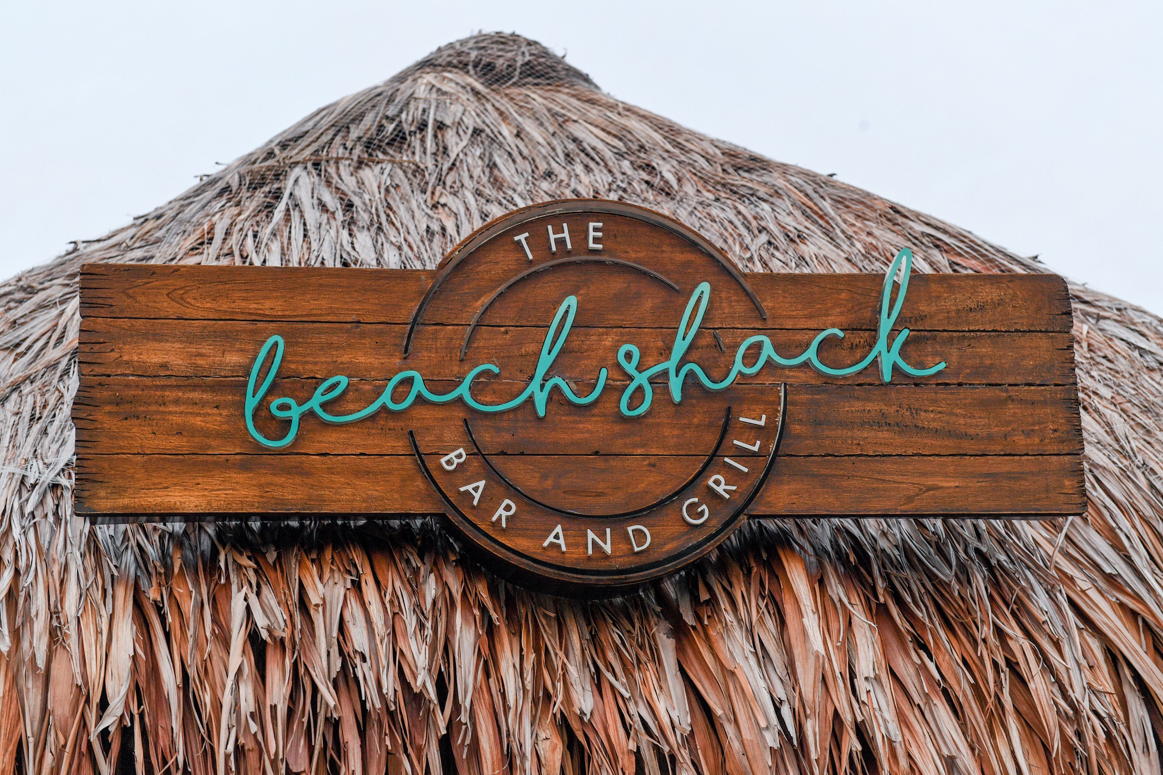 A wooden sign with the words "The Beach Shack Bar and Grill" on a thatched roof.
