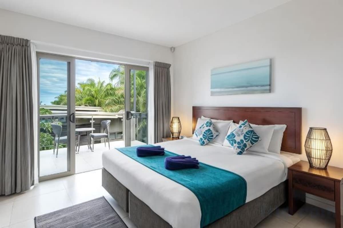 A hotel room with a bed, a balcony, a painting, and a nightstand.