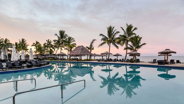 A pool area with lounge chairs, umbrellas, and palm trees. - Club Wyndham Denarau Island, Trademark Collection by Wyndham (Nadi)