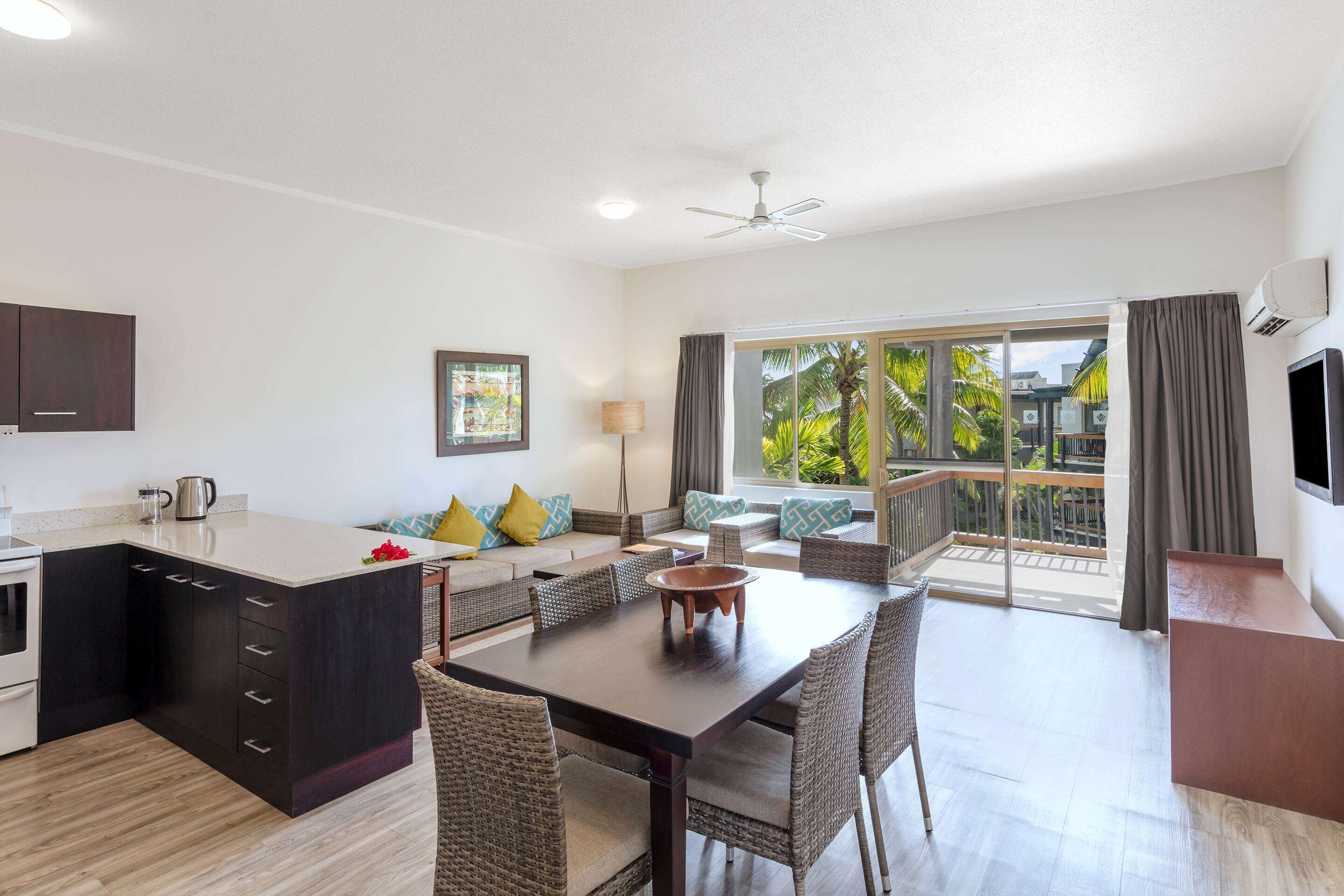 A modern kitchen with dark cabinetry, a central island, and a dining area with wicker chairs.