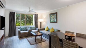 A modern living room with a sofa, a coffee table, a dining table with chairs, a ceiling fan, and a large window with curtains. - Club Wyndham Denarau Island, Trademark Collection by Wyndham (Nadi)