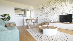 Un salon moderne comprenant un coin repas, une grande fresque murale, un téléviseur à écran plat et une table basse ronde.