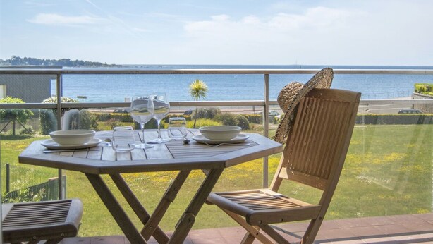 Une table en bois, agrémentée d’un verre et d’un bol, une chaise en osier et une vue sur la mer.