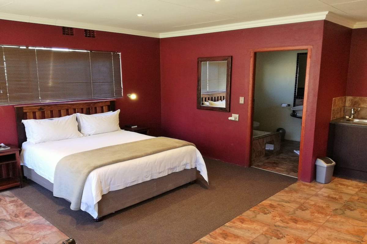 Een slaapkamer met een bed, een nachtkastje, een spiegel en een zichtbare badkamer door een geopende deur.