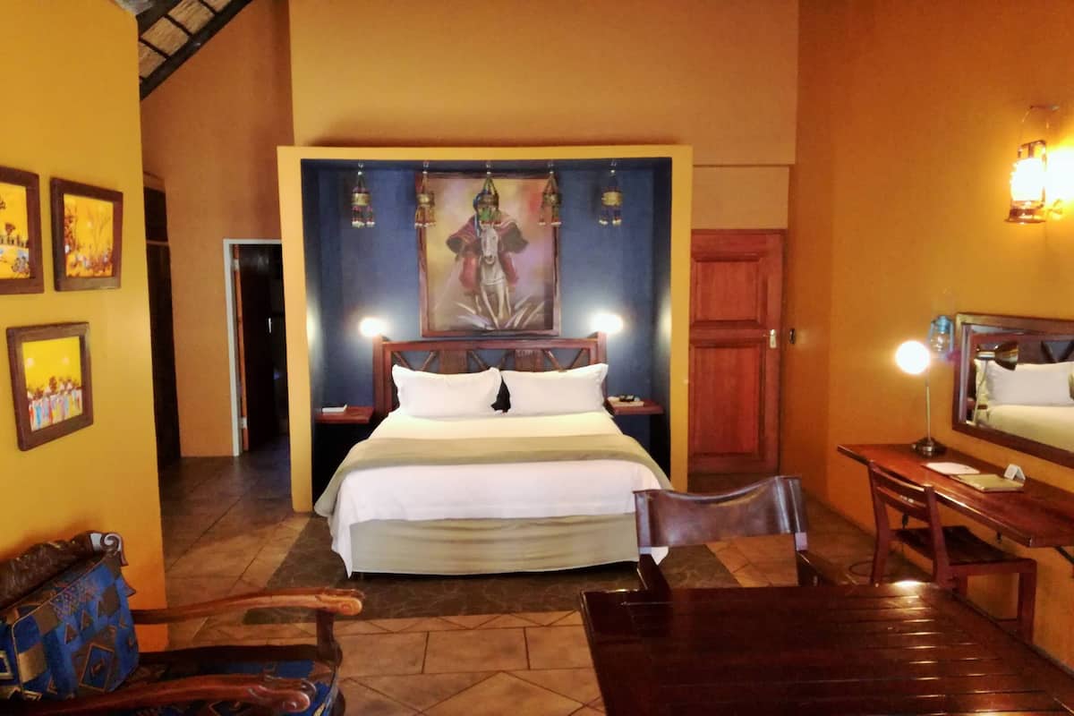 Een hotelkamer met een bed, nachtkastje, stoel, bureau, lamp en een schilderij aan de muur.