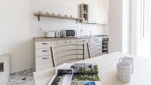 A modern kitchen with white cabinetry, a microwave, a kettle, and a gas stove. There are two chairs and a table with a magazine and mugs. - Italianway - Ripa Ticinese 103 (Milan)
