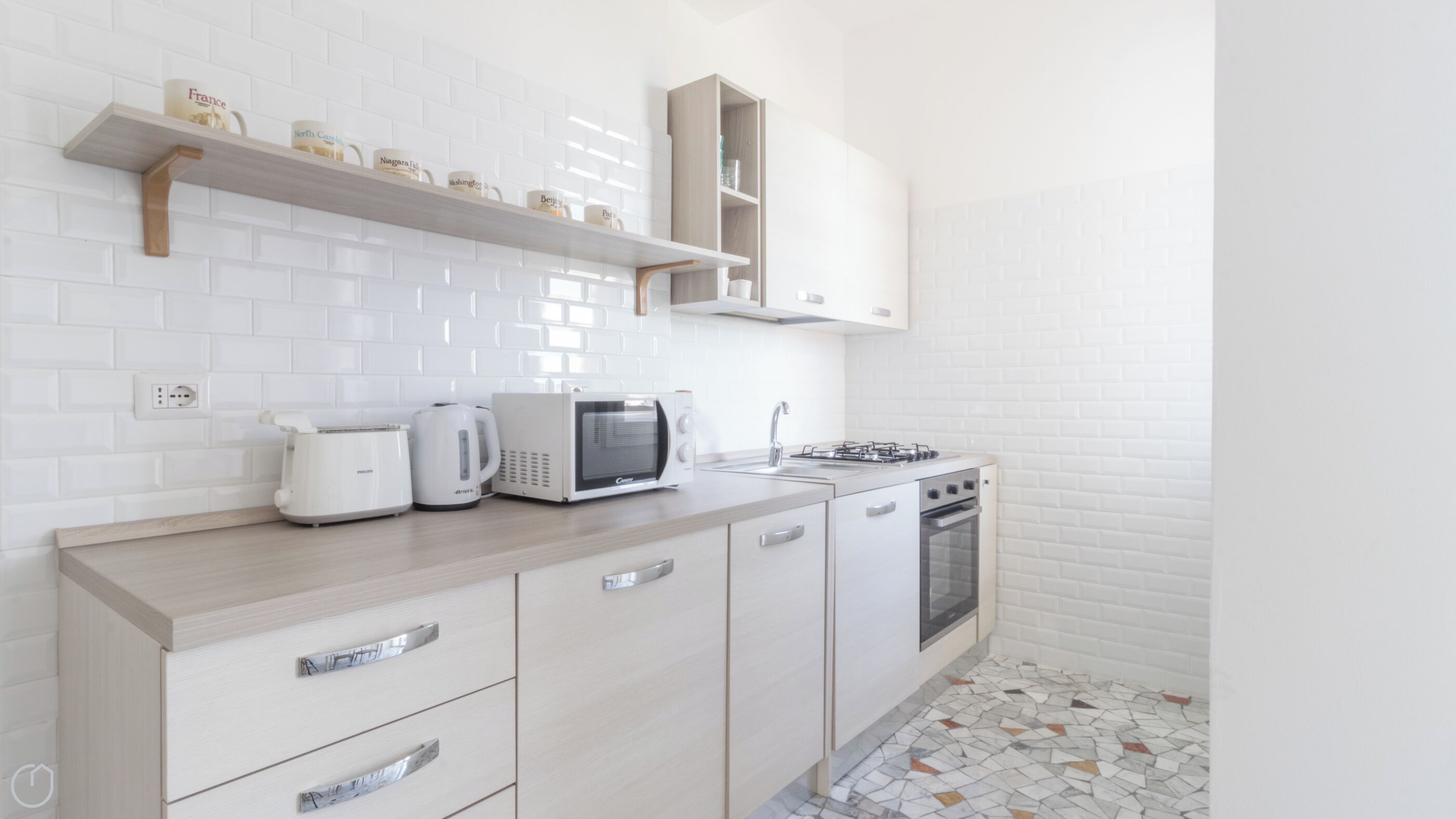 Une cuisine moderne avec des meubles blancs, un four à micro-ondes, une bouilloire et une cuisinière à gaz.