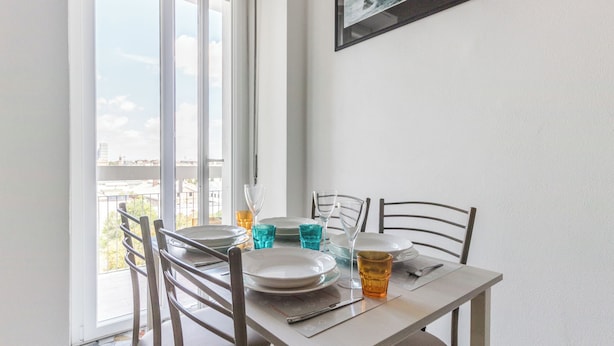 A dining area with a table set for two, chairs, and a window with a view of buildings. - Italianway - Ripa Ticinese 103 (Milan)