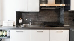 A modern kitchen with white cabinets, a stainless steel sink, and a black tiled backsplash. - Italianway - Corsica 61 (Milan)