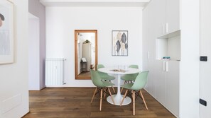 A modern dining area with a round table and four green chairs, a white cabinet, and a mirror reflecting the room. - Italianway - Corsica 61 (Milan)
