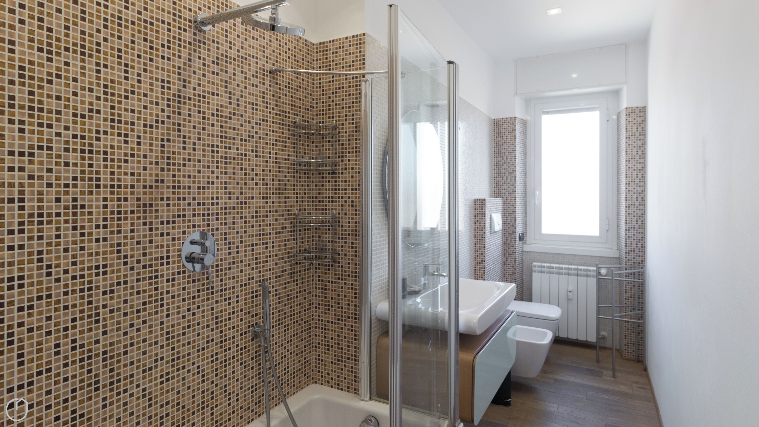 A modern bathroom with mosaic tile walls, a glass shower enclosure, a white bathtub, and a window providing natural light.