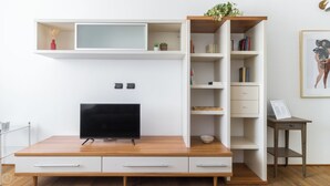 A modern living room with a flat-screen TV on a wooden TV stand, white built-in shelves with books and decorative items, and a small side table with a framed picture. - Italianway - Corsica 61 (Milan)