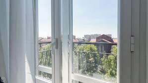 A view from a window with white frames and a balcony railing, overlooking a cityscape with buildings and trees. - Italianway - Corsica 61 (Milan)