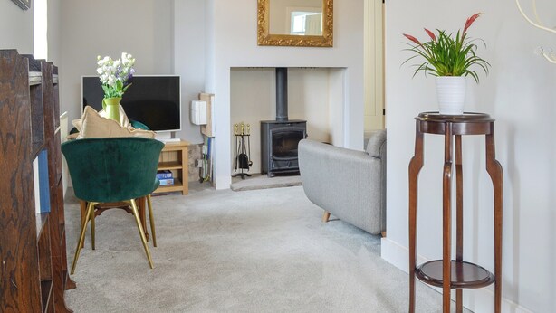 Una sala de estar con un sofá, una silla verde, un aparador de madera, un televisor, una chimenea y una planta en maceta.