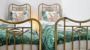 Dos camas individuales con ropa de cama floral, una mesita de noche con lámpara y vistas al cielo a través de una ventana.