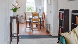 Un comedor con una mesa dispuesta para cuatro personas, una planta en maceta y una estantería.