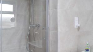 Un baño moderno con cabina de ducha de vidrio, un lavamanos blanco y una botella de jabón Carex.