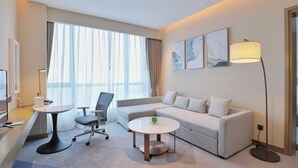 Una habitación de hotel moderna con sofá, una mesa redonda, un escritorio y una lámpara.