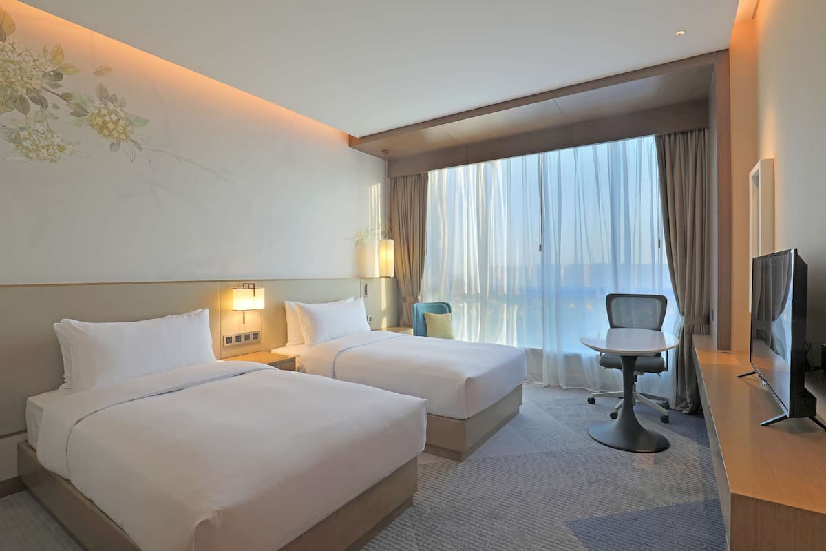 A hotel room with two beds, a desk, a chair, and a TV.