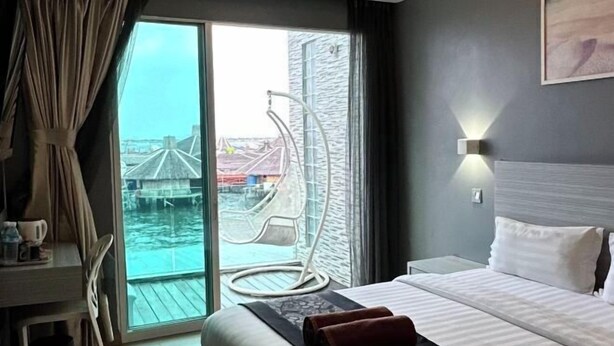 Ein Hotelzimmer mit Bett, Schreibtisch mit Stuhl, großem Fenster mit Blick auf ein Gewässer und eine Brücke sowie einer Wandleuchte.