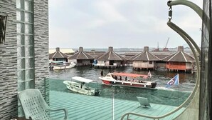 Blick aus einem Zimmer mit Fenster auf ein Gewässer, auf dem Bungalows direkt im Wasser stehen und ein Boot fährt.