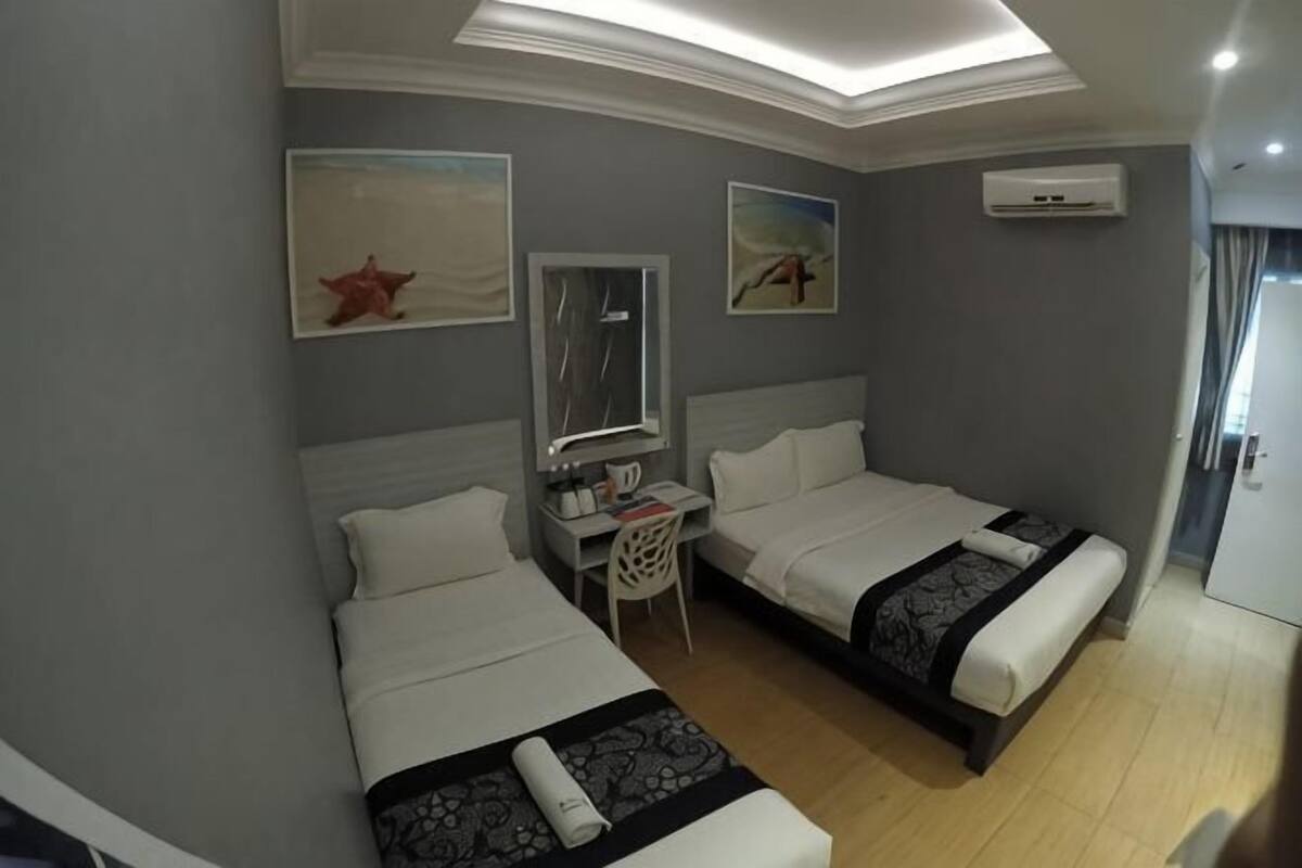 A hotel room with two beds, a desk, a chair, a small table, a mirror, and artwork on the walls.