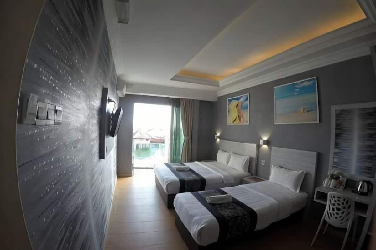 A hotel room with two beds, a TV, a desk, and a view of the outdoors.