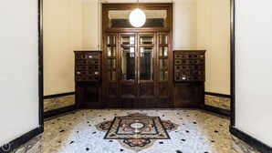 Un couloir doté d’un sol à motifs, une porte en bois avec des panneaux de verre, et deux armoires en bois avec des tiroirs.