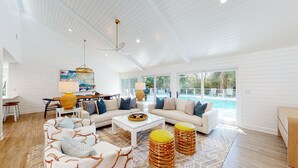 Ein großzügiges Wohnzimmer mit weißer Decke, großen Fenstern, einem Pool und einem Essbereich.