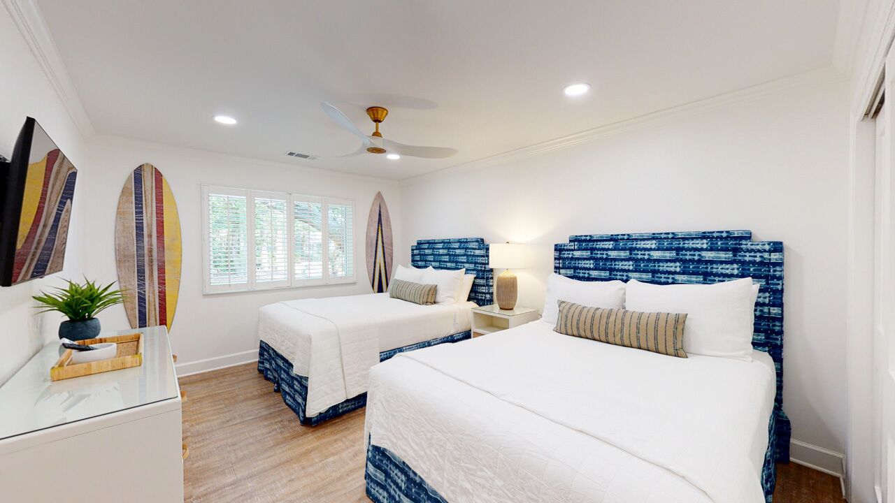 A hotel room with two beds, a ceiling fan, a nightstand, and surfboards on the wall.