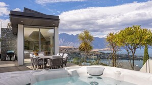 Een moderne buitenjacuzzi met een eethoek en een glazen constructie met uitzicht op een bergachtig landschap.