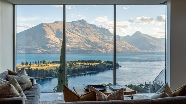 Een woonkamer met een groot raam met uitzicht op een meer en bergen.