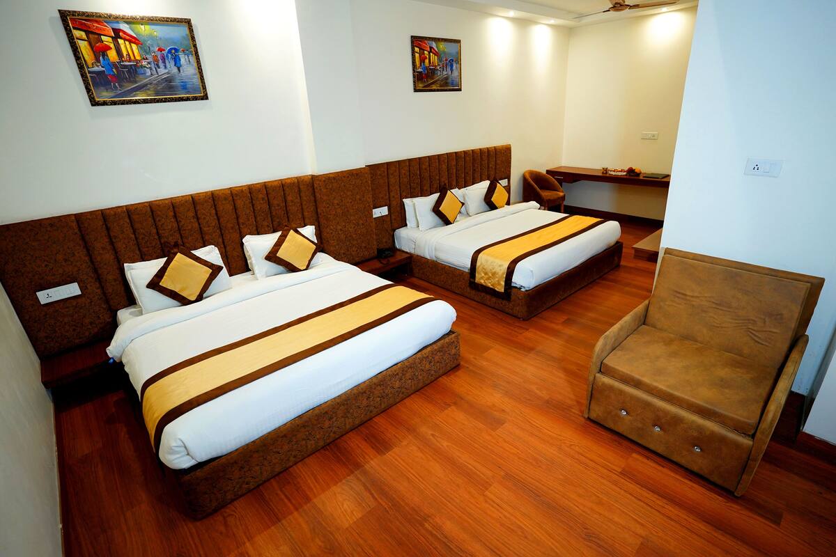 Habitación de hotel con dos camas, suelo de madera y un sillón marrón.