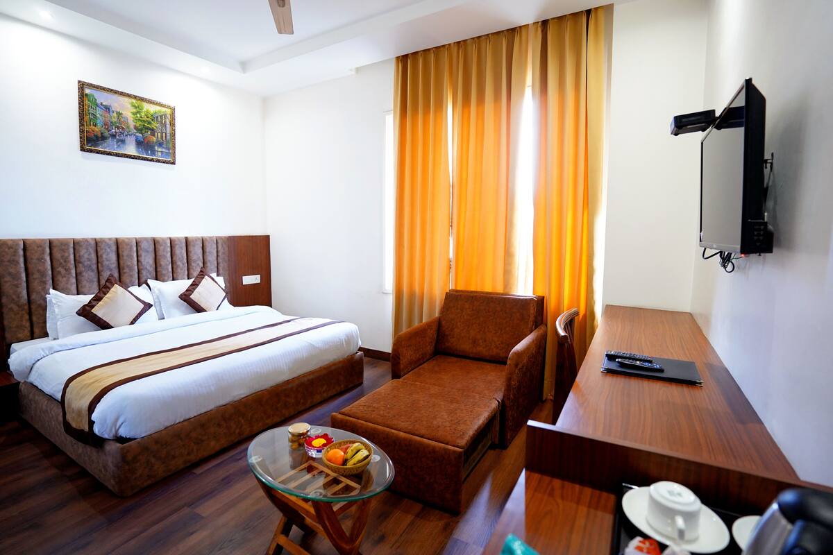 Habitación de hotel con cama, sofá, escritorio, televisor y un cuadro en la pared.