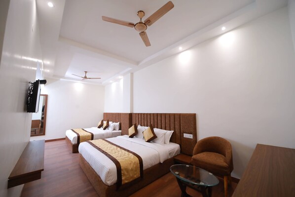 Une chambre d’hôtel avec deux lits, un canapé, une table en verre et des ventilateurs de plafond.