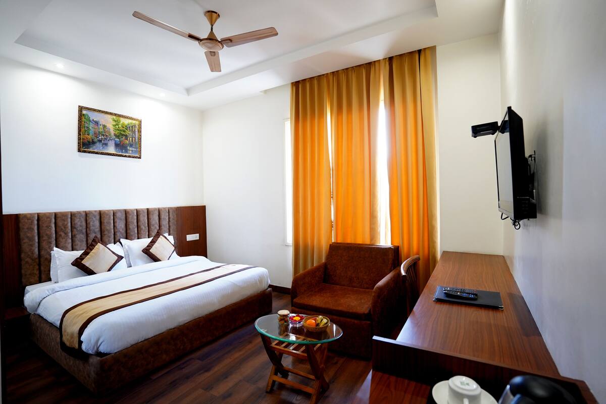 Una habitación de hotel con una cama, una silla, una mesita con frutero, un televisor y un ventilador de techo.