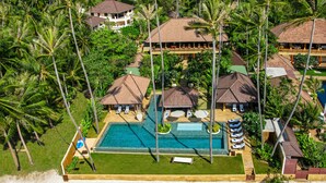 Vista aérea de um resort com várias construções no estilo de bangalôs, uma piscina central e vegetação tropical exuberante.