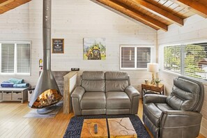 A cozy living room with a fireplace, leather sofas, and a wooden ceiling.