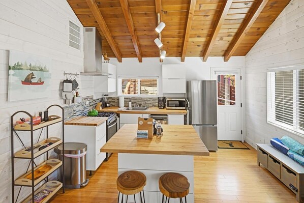 A modern kitchen with wooden beams, white cabinetry, a central island, and bar stools.