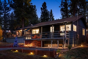 A two-story cabin with a balcony, a deck, and a Christmas tree.