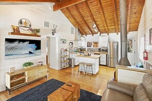 A modern interior with a wooden ceiling, a kitchen area, a seating area with a sofa and coffee table, and a television mounted on the wall.